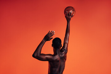 Back view of unrecognizable African American male athlete throwing basket ball against an orange...