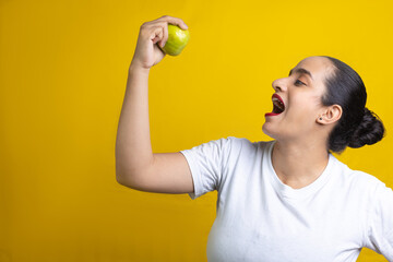 Hispanic woman about to bite green apple, in yellow background