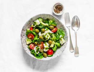 Fresh vegetable salad with tomatoes, avocado, lettuce, cucumbers, burrata and pesto sauce dressing on a light background, top view