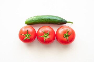 Three red ripe tomatoes with one green cucumber above them