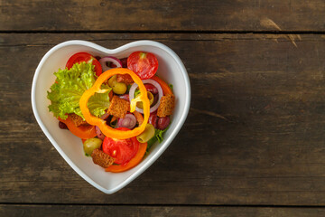 Vegetable salad in a heart shape plate on a wooden table.