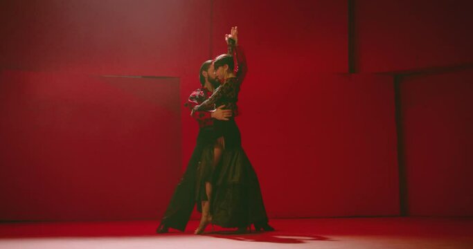 4K Beautiful couple dancing latin dance . Professional dancers dancing flamenco, rumba or salsa on red background. Pair in spanish dress performs dance movement. Shot ARRI ALEXA Camera in Slow Motion