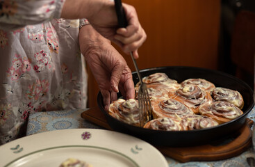 Hands and buns close-up.happy old woman Granny cooks in kitchen cinnamon rolls and bakes cookies. Portrait, selective focus, low key