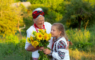 Gray haired grandmother and girl granddaughter both wearing embroidered shirts with a bouquet of sunflowers smiling snd happy. Independence day, constitution of ukraine