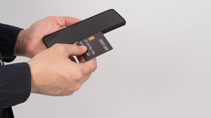 Hand is holding mobile phone and black credit card on white background.