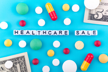 health care is for sale written on cubes, around them pills and pills and paper bills