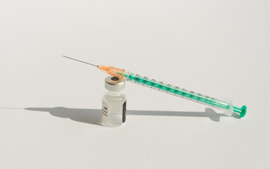 Close-up dose vaccine vial and injection syringe on a white background. The bottle and syringe cast a harsh shadow. Coronavirus vaccination concept. - obrazy, fototapety, plakaty