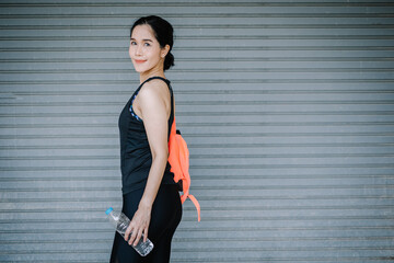 A woman wearing a cute fitness outfit holds a water bottle with a smile and looks straight at the camera. concept of health care and drinking clean water