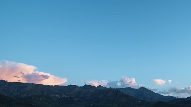 Day to night to day holy grail time-lapse of clouds and the milky way passing over the mountains of Monte San Parteo and Monte Grosso and the village of Speloncato in the Balagne region of Corsica