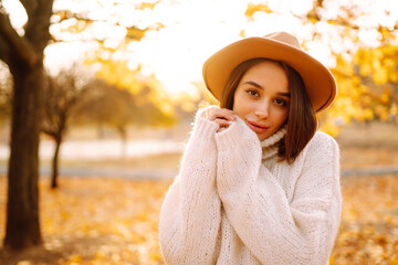 Autumn woman. Young cheerful woman in white sweater and hat walks in the nature park on a sunset. Fashion, style concept.