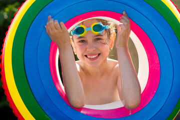 A happy little girl in swimming glasses and a colorful inflatable ring