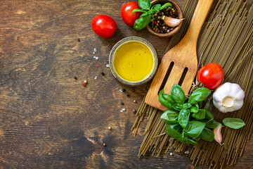 Ingredients for italy cuisine. Spinach spaghetti, herbs, spices, olive oil and tomatoes on a rustic table. Top view flat lay background. Copy space.