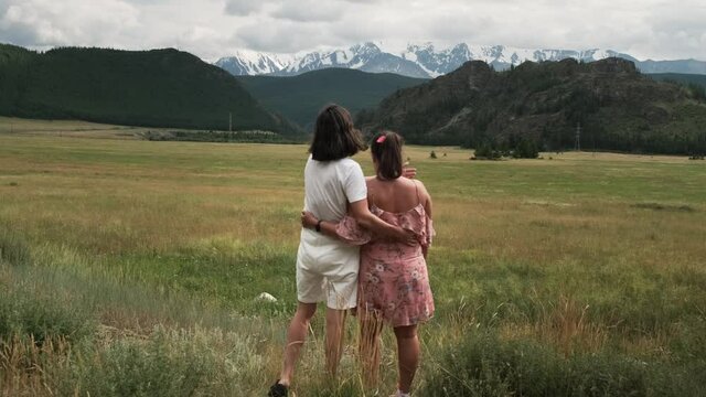 Two young girls are relaxing in nature, holding hands and hugging each other against the backdrop of beautiful mountains. LGBT, sexual minorities. 