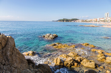 Rocky coast and sandy beach of the small Spanish resort of Lloret de Mar on a sunny summer day.