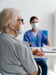 Obraz premium woman doctor sitting at the table and elderly patient wearing a medical mask health covid passport