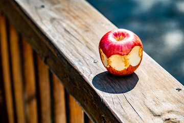 Half-eaten apple with three bites sitting outside on a wooden railing