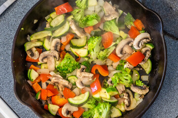 Stir fry vegetables with mushrooms, broccoli, zucchini, and peppers in cast iron pan