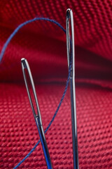 two sewing needles with blue thread on a background of red fabric. close-up.
