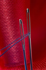 two sewing needles with blue thread on a background of red fabric. close-up.