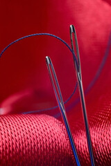 two sewing needles with blue thread on a background of red fabric. close-up.