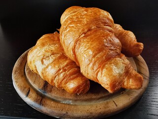 The croissant lies on a round wooden board on the black table.