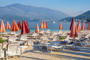 Beautiful Mediterranean landscape with beach umbrellas. Beach vacation concept. Montenegro, Adriatic Sea. View of Kotor Bay near Tivat city on sunny August morning
