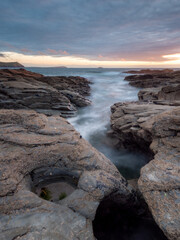 Fototapeta na wymiar Water streaming into a channel in the slate ledges of the North Cornwall coast at sunset