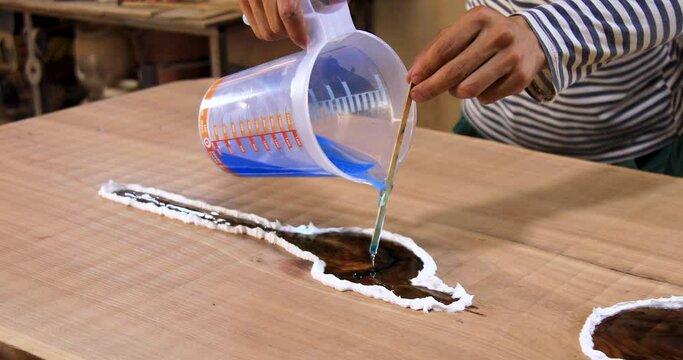 Closeup of carpenter pouring liquid epoxy in a wooden table