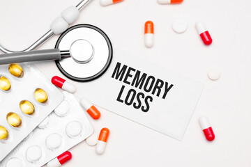 Stethoscope, pills and notebook with Memory Loss word on medical desk.