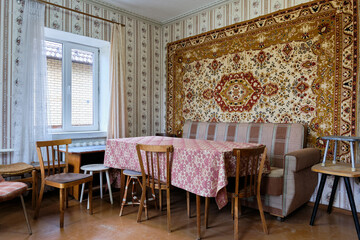 Example of Old Soviet Russian poor interior in Khruschev House. Aged  sideboard, table, chairs, sofa. Shabby floor. Tattered wallpaper on the wall. Paper butterflies as decor. Apartment of pensioners.