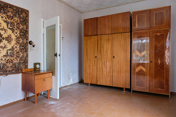 Example of Old Soviet Russian poor interior in Khruschev House. Aged  sideboard, table, chairs, sofa. Shabby floor. Tattered wallpaper on the wall. Paper butterflies as decor. Apartment of pensioners.
