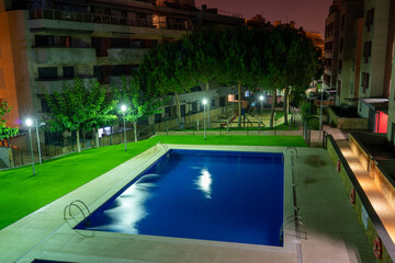 Swimming pool at night with some lights and greens around it
