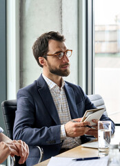 Serious Caucasian bearded male ceo wearing suit looking at colleague discussing corporation strategy project at table. Focused ceo manager leader working in modern office. Vertical. - obrazy, fototapety, plakaty