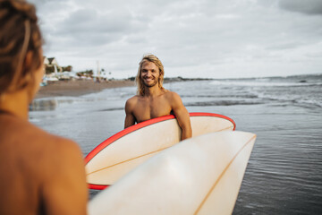 Long-haired man with smile looks at girl. Couple is going to surf
