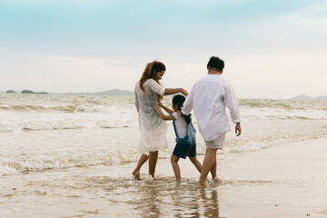 Asian father and mother play with child and walking along the beach
