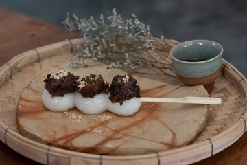 Dango small round Mochi balls skewed on bamboo sticks put in natural rock plate with Japanese hot tea