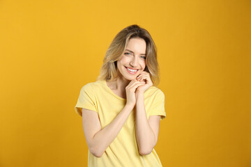 Portrait of happy young woman with beautiful blonde hair and charming smile on yellow background