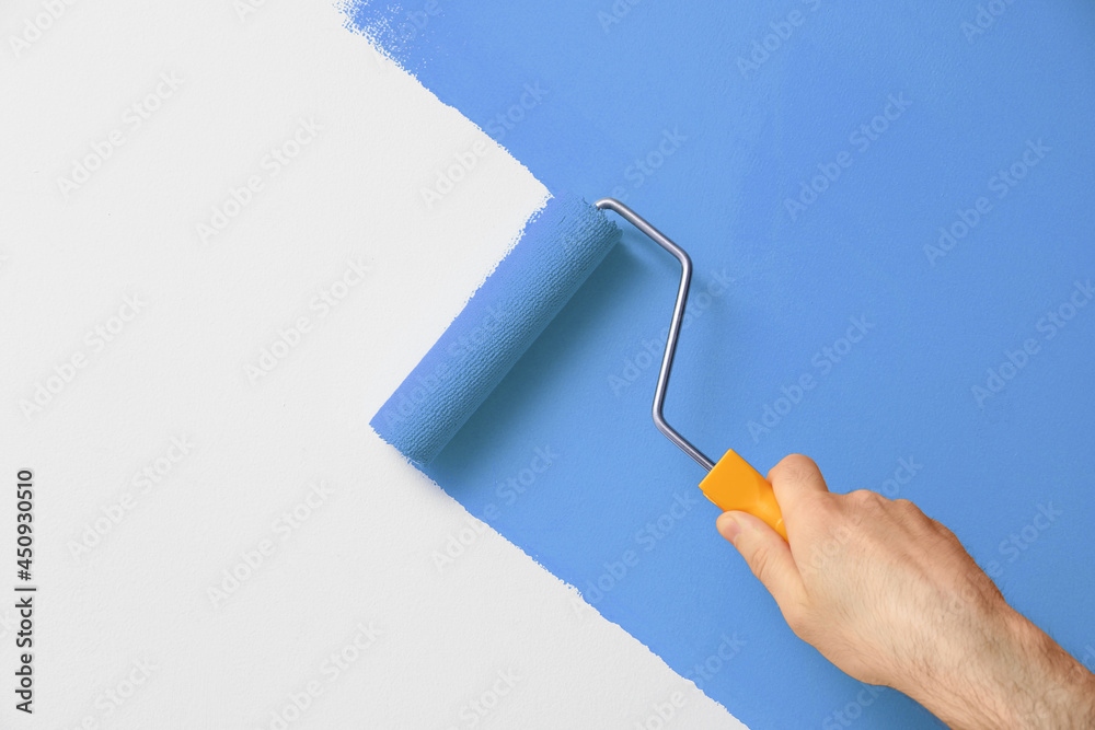 Canvas Prints Man applying orange paint with roller brush on white wall, closeup