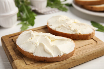 Bread with cream cheese on wooden table, closeup