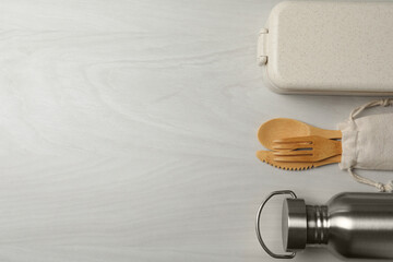 Lunch box, metal bottle and bamboo cutlery on white wooden table, flat lay with space for text....