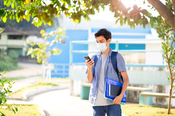 College student returning to college or school and wearing a mask to protect himself from Covid-19. Using cell phone while walking on college campus.