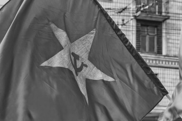 Soviet red waving flag with hammer and sickle on the background of the soviet building in black and white