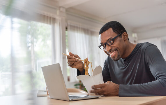 African American man eating noodle with his friends while having video chat on laptop