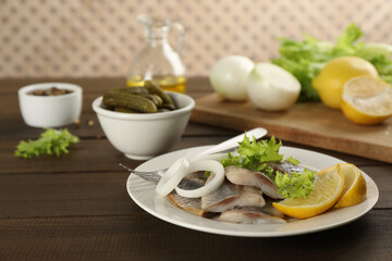 Sliced salted herring fillet served with lettuce, onion rings and lemon on wooden table