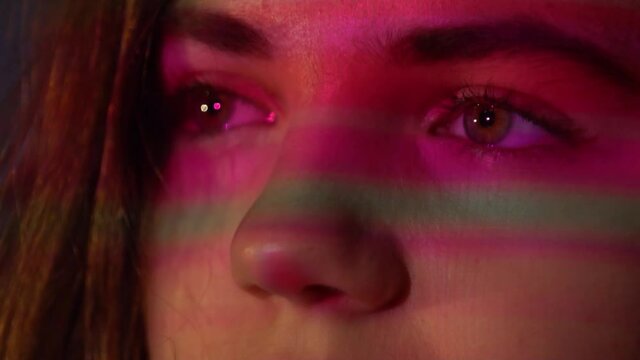 Extreme close up of Beautiful young womans face while looking at Camera with Projector Reflection on her face. Slow motion