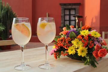 Classic Gin drink cocktail shaked with grapefruit in elegant glasses next to colorful flowers on an elegant table
