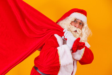 Santa Claus on yellow background holding bag with gifts with free space for text behind his back....
