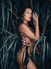 Young sexy brunette woman savage in leopard print pattern bikini standing sideways at, hiding...