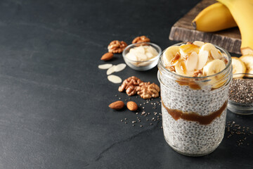 Delicious chia pudding with banana, walnuts and caramel sauce on black table, space for text
