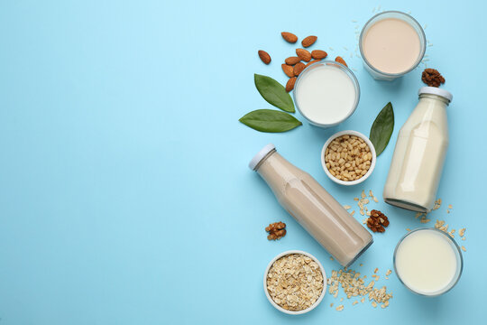 Different vegan milks and ingredients on light blue background, flat lay. Space for text